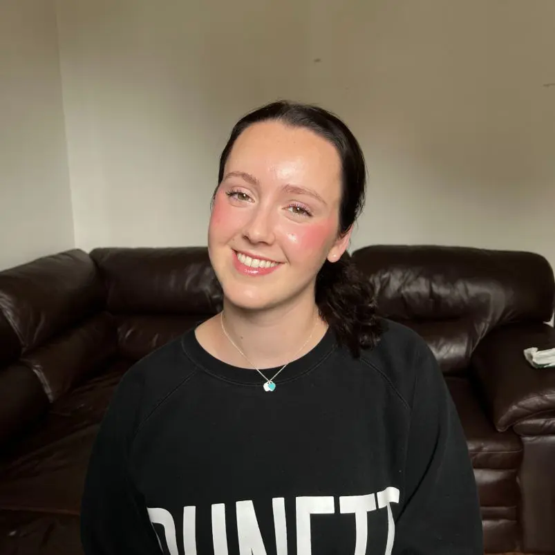 Smiling person sitting on a dark sofa.