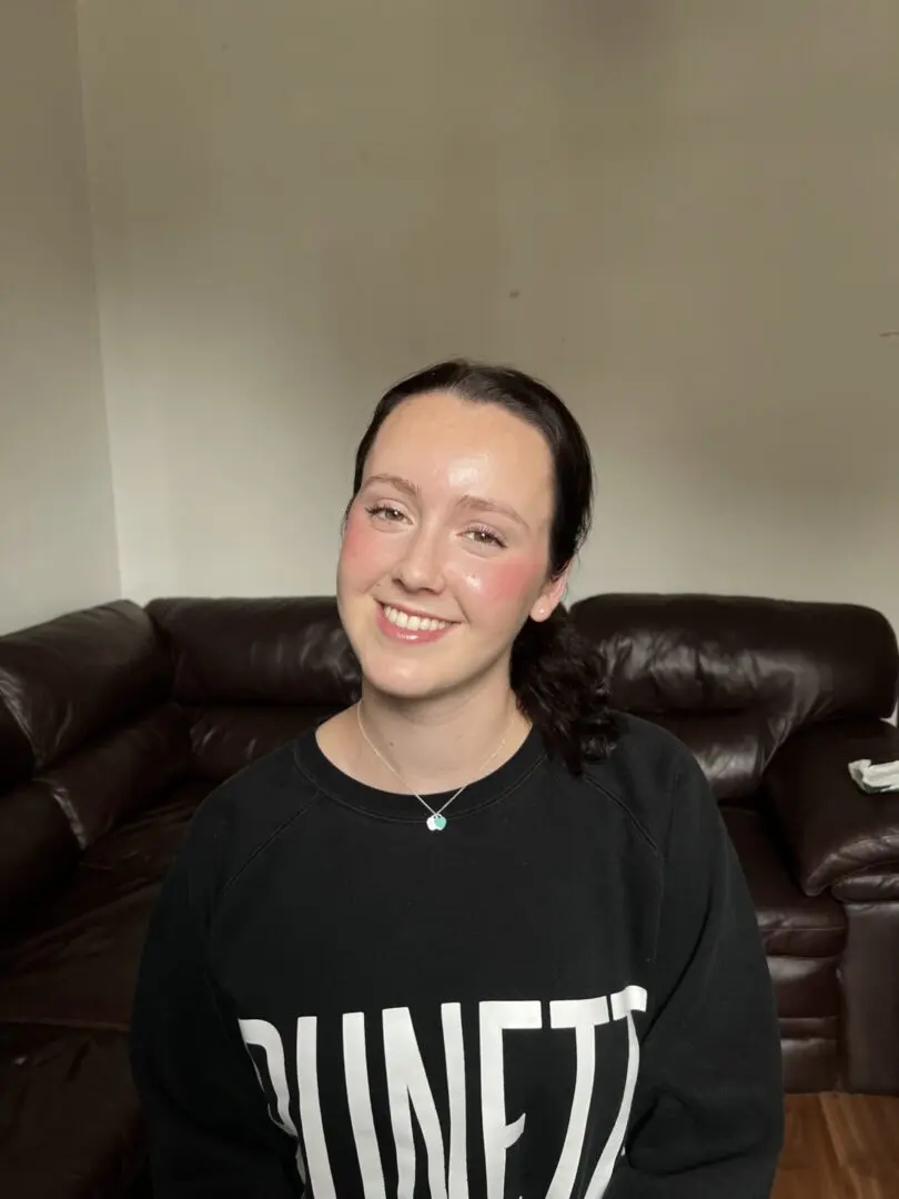 Smiling person sitting on a brown couch.